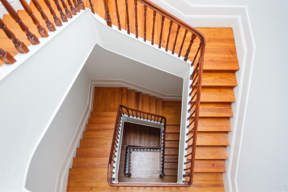 A view from the top of a wooden staircase inside a residential property, showing the spiral layout with multiple turns descending towards the ground floor. The stairs are made of polished oak with mat